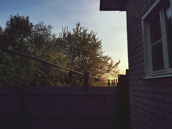 Low angle view of silhouette tree by building against sky