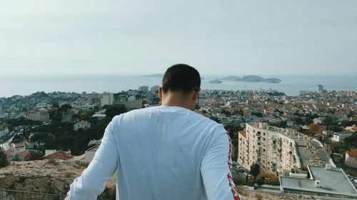 Rear view of man looking at city buildings against sky