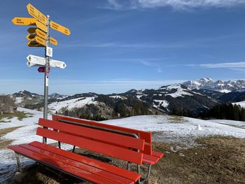 Information sign on snowcapped mountains against sky with red bench in the foreground