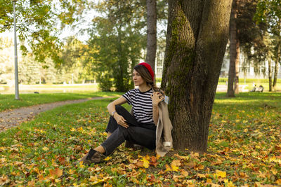 Full length of teenage girl sitting on tree trunk