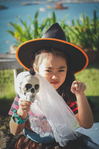 Portrait of girl wearing witch hat holding skull