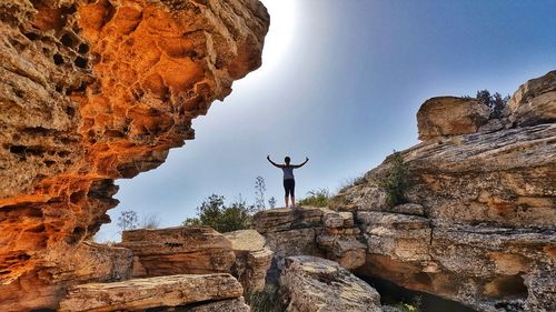 Low angle view of woman standing on rock against sky