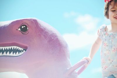 Close-up of girl with dinosaur sculpture against sky