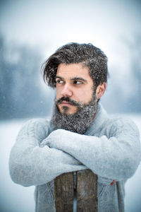 Young bearded man with arms crossed standing during snowfall