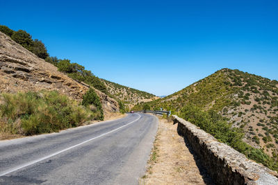 Empty road along landscape against clear blue sky