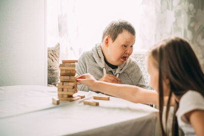 Elderly woman with down syndrome and an asian girl play in tower from wooden blocks