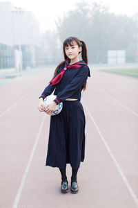 Full length of woman holding ball while standing on road