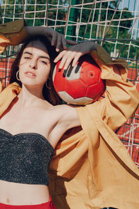 Portrait of smiling young woman holding soccer ball standing by goal