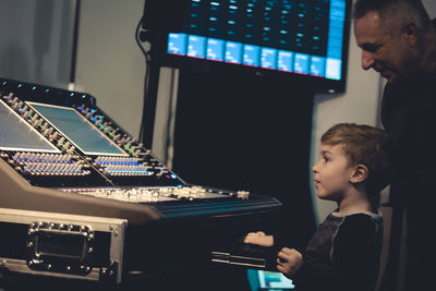 Music teacher and boy standing by sound mixer at recording studio