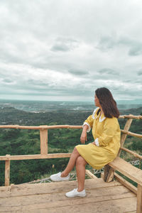 Full length of woman sitting on railing against mountains