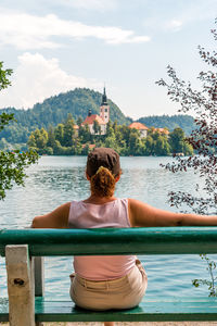 Woman tourist sitting on a bench with her back turned, looking out over lake bled in slovenia.