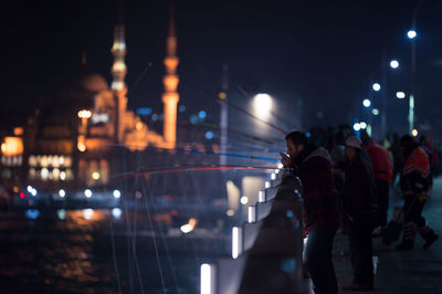 People fishing on illuminated galata bridge at night