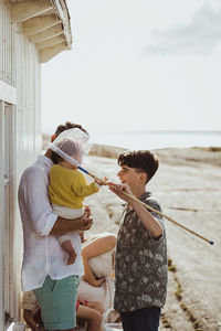 Side view of playful brother covering sister's head with fishing net by cabin