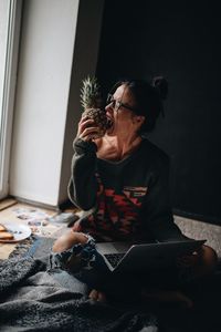 Woman eating pineapple while using laptop while siting at home