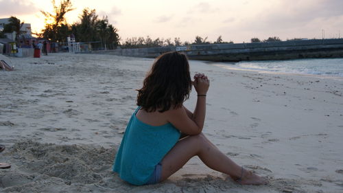Young woman sitting at beach against sky during sunset