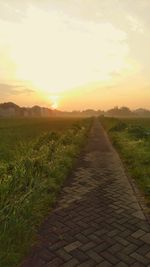 Footpath amidst field against sky during sunset