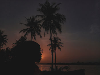 Silhouette palm trees on beach against sky at sunset