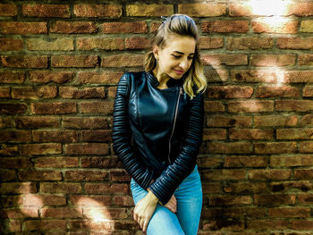 Young woman standing against brick wall