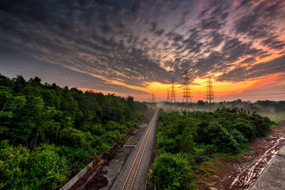 Railway tracks amidst trees against sky during sunset