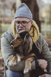 Man embracing dog while crouching at park during autumn