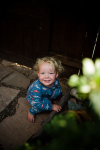 Toddler in pajamas smiling for camera while crouching in front yard