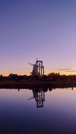 Silhouette factory by lake against clear sky during sunset