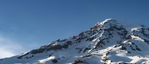 Low angle view of snowcapped mountains against clear blue sky