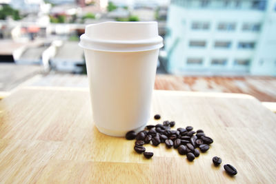 Close-up of disposable cup and coffee beans on table