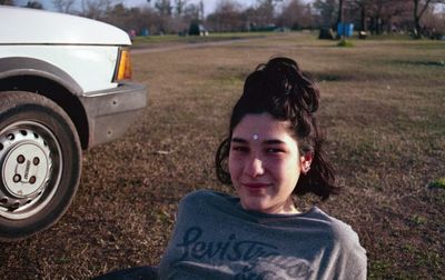 Portrait of smiling young woman sitting by car at park