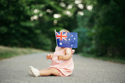 Cute girl holding australian flag sitting on road