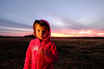 Portrait of girl standing on field against sky during sunset