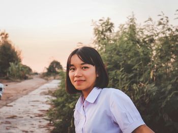 Portrait of smiling woman standing against trees during sunset