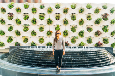 Full length portrait of young woman standing against wall