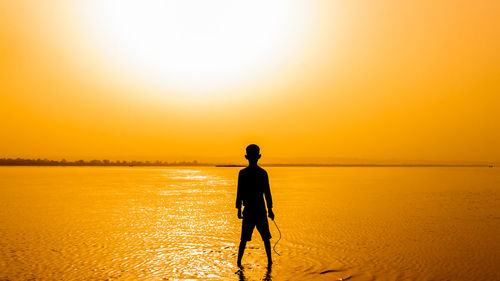 Silhouette man standing on beach against sky during sunset