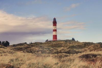 Lighthouse on field by building against sky