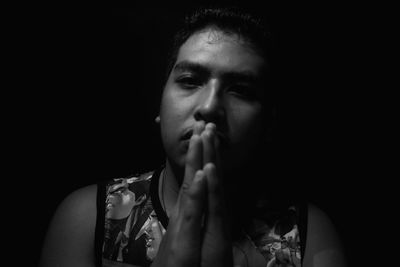 Portrait of young woman with hands clasped against black background