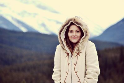 Portrait of smiling young woman in warm clothing standing on landscape against sky