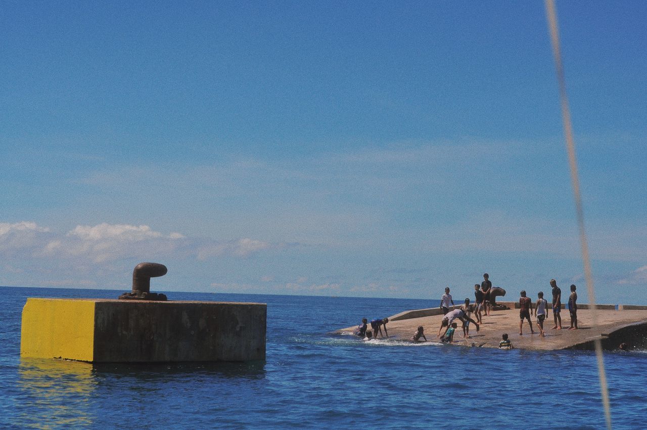 PEOPLE ON BEACH BY SEA AGAINST BLUE SKY