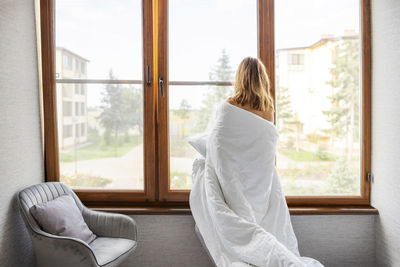 Rear view of woman looking through window at home