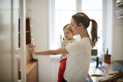 Female influencer taking selfie with daughter through smart phone at home