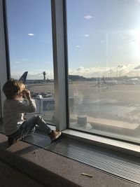 Woman sitting by window against sky