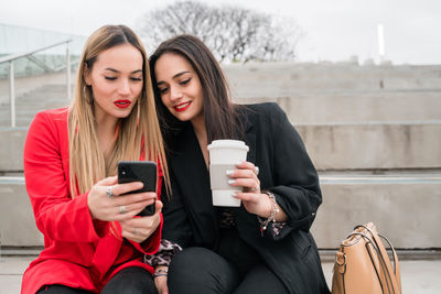 Young woman using smart phone while sitting on laptop