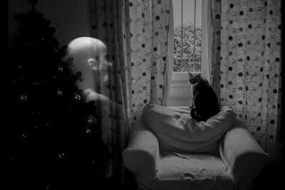 Double exposure of woman by curtain and cat sitting on armchair at home