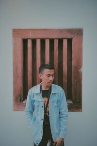 Young man looking away while standing against wall