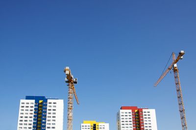 Low angle view of crane by building against clear blue sky