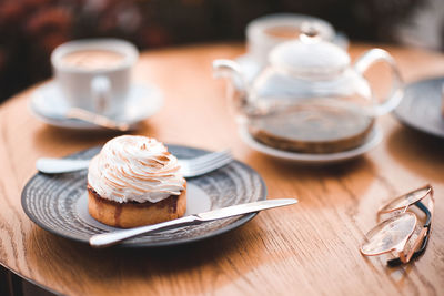 Delicious creamy cake with teapot and cup of tea on wooden table in cafe closeup.