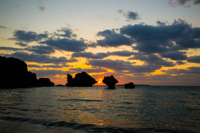 Silhouette rocks in sea against sky during sunset