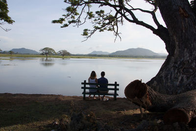 Men sitting by lake against sky