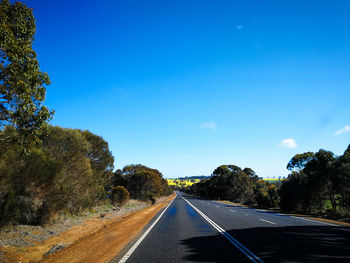 Empty road amidst trees against blue sky in western australia.