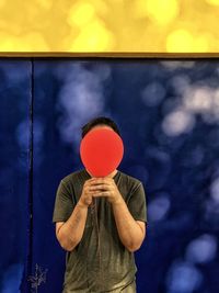 Man holding red balloon against blue and yellow wall.